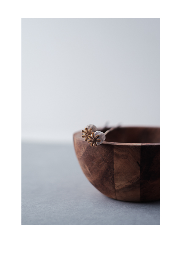 Asetelma puukulhosta ja unikoiden siemenkodista. Valokuva.