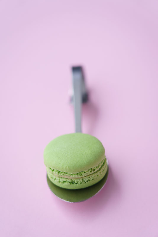 Värisuunnittelukuva, jossa vihreä macarons vaaleanpunaisella taustalla. Valokuva.